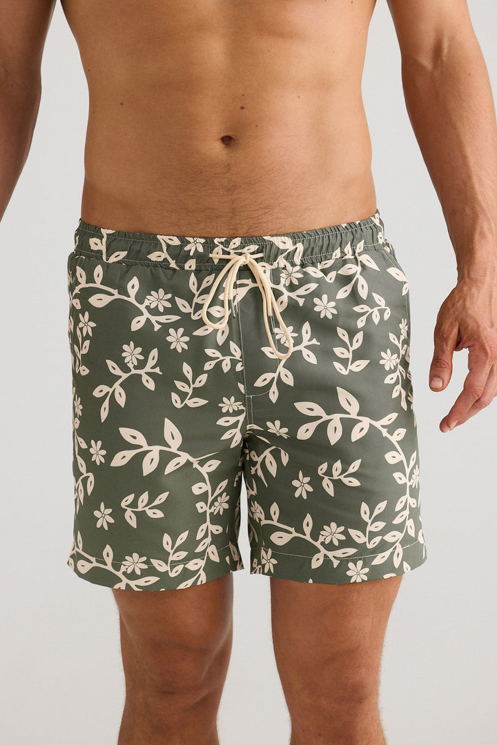 Man wearing green floral-patterned shorts on a plain background