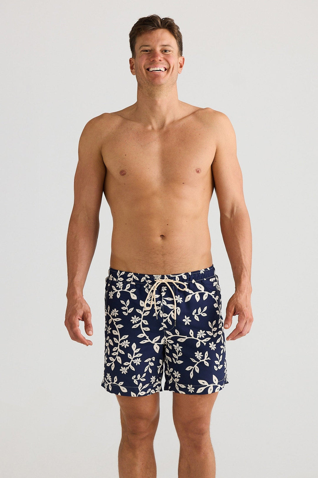 Man wearing navy swim shorts with a white floral pattern on a plain background