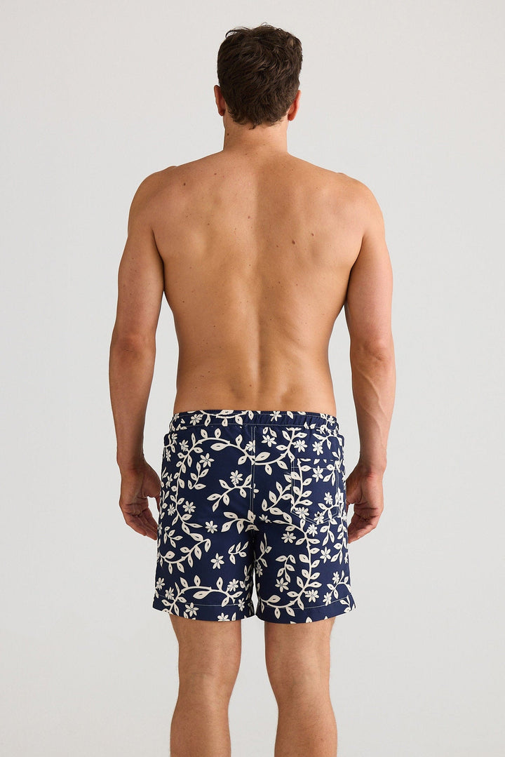 Man wearing navy blue swim shorts with a white floral pattern on a plain background
