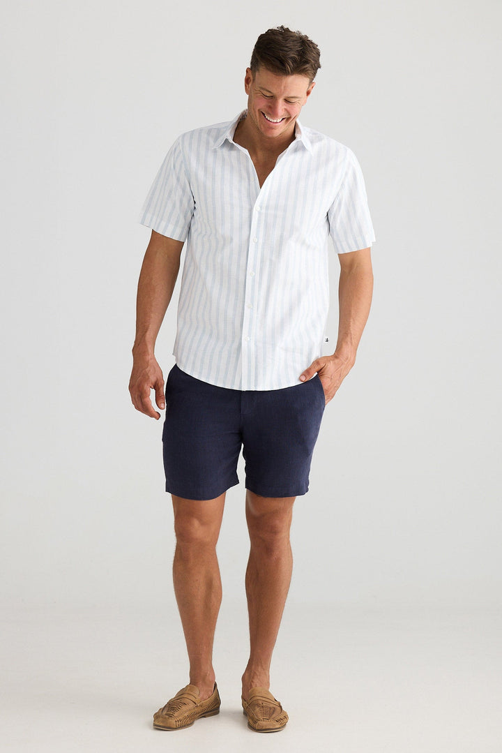 Man wearing a white striped shirt and navy shorts on a light gray background