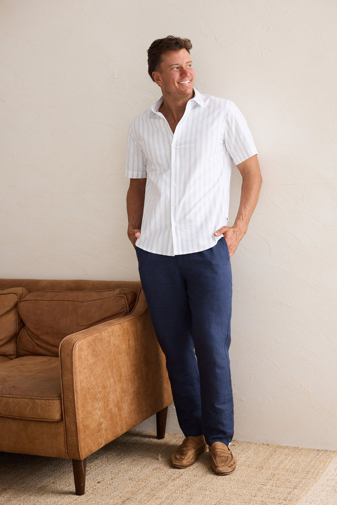 Man wearing a white shirt and blue pants standing in a room with a brown couch.