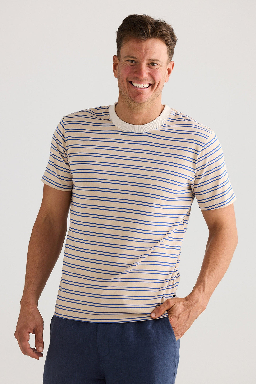 Man wearing a striped t-shirt and navy pants against a plain background