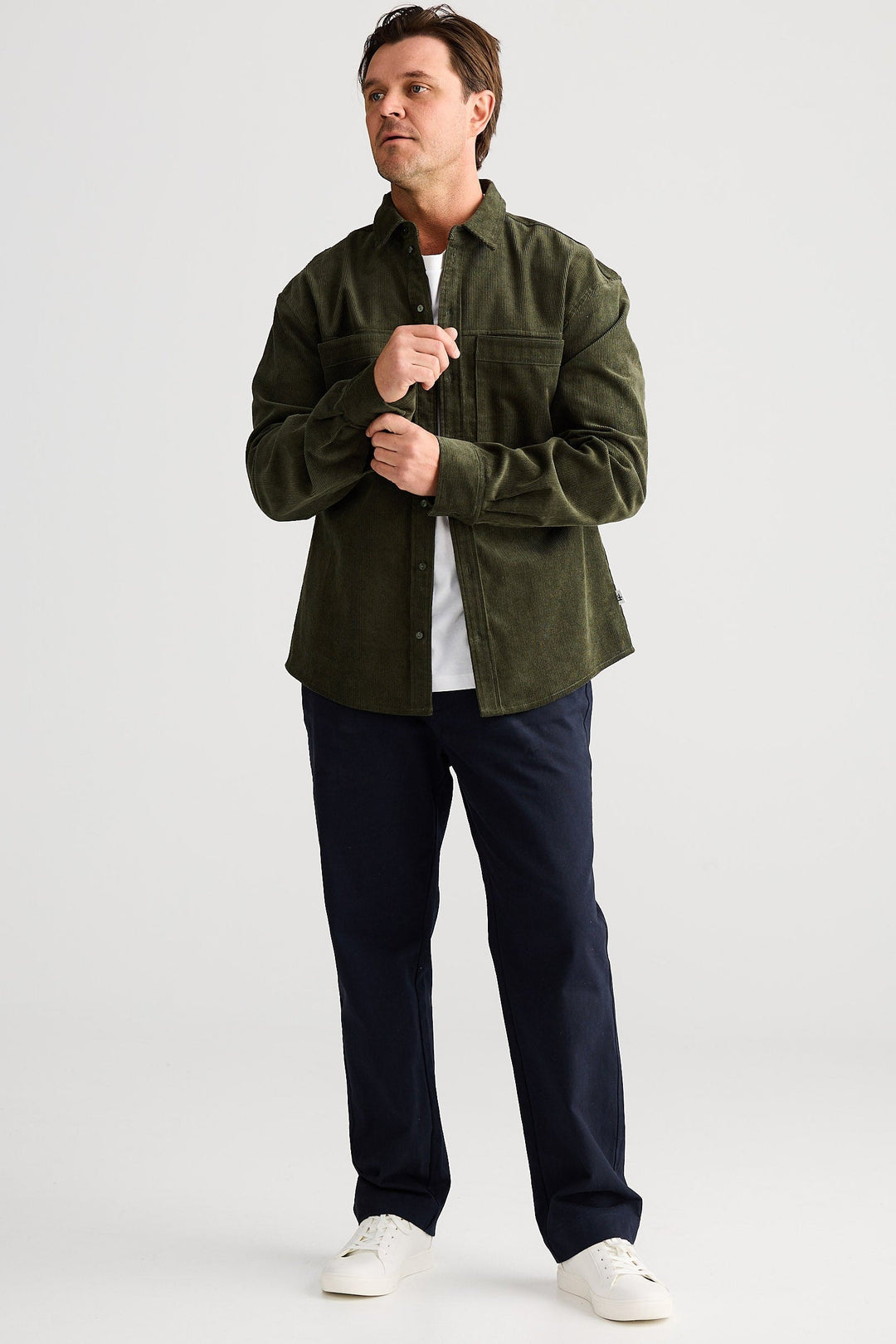 Man wearing a green jacket, white shirt, and dark pants on a light gray background