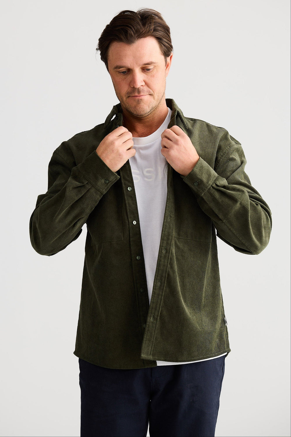 Man wearing a green jacket over a white shirt on a light gray background