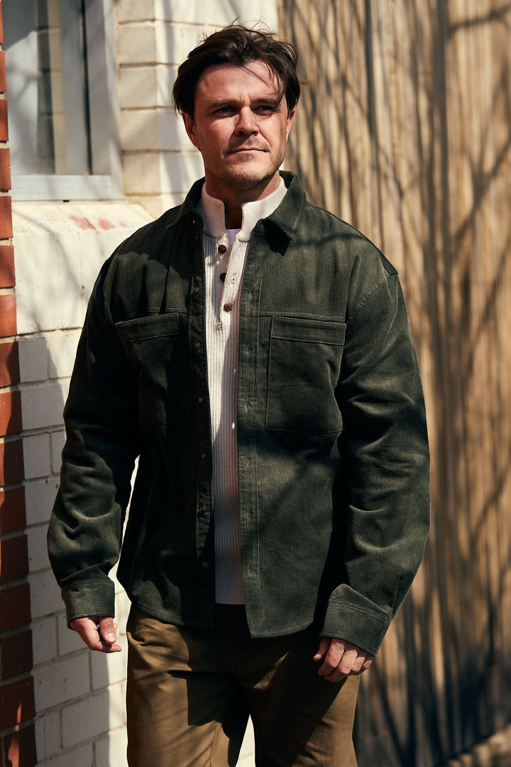 Man wearing a green jacket standing against a brick wall.