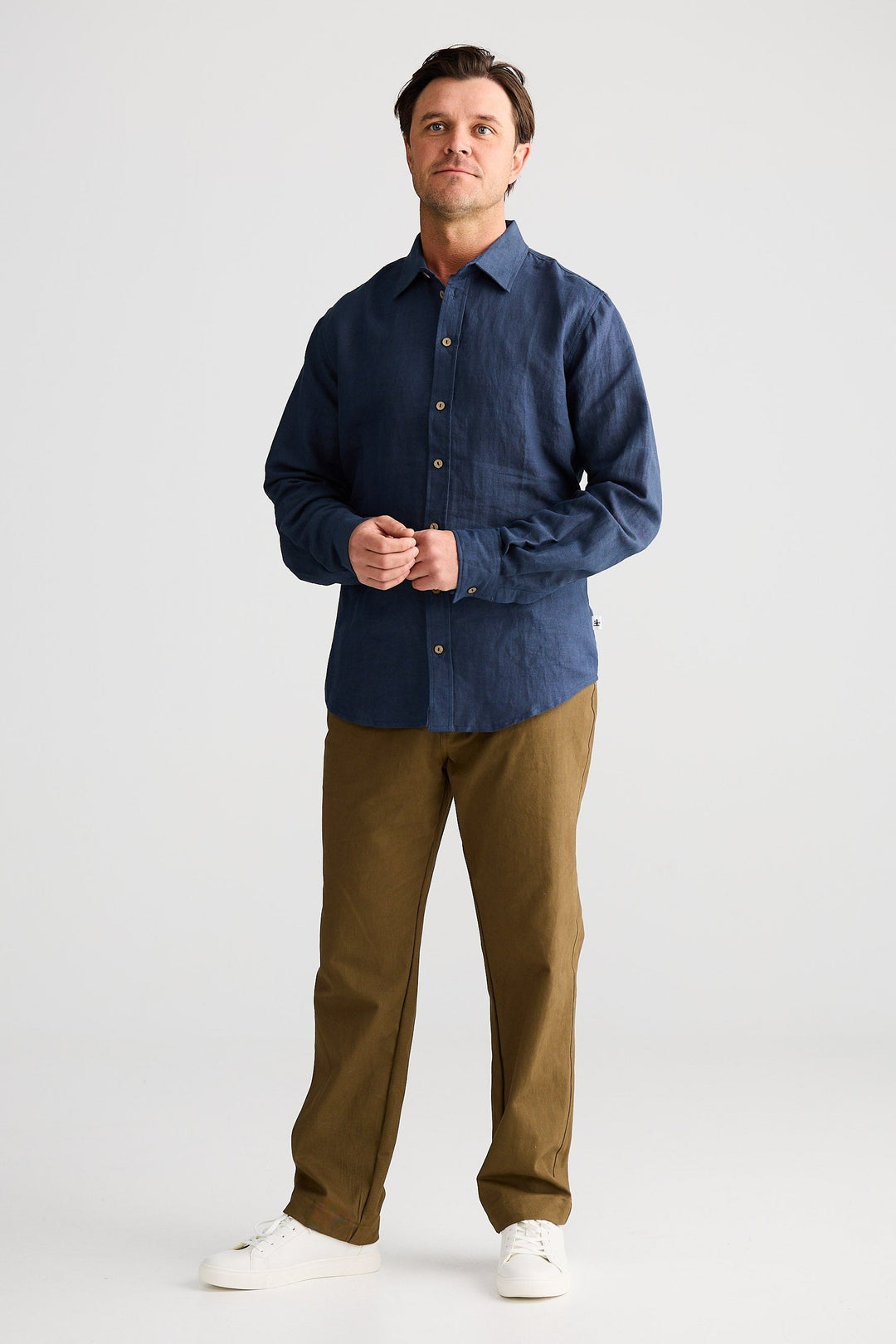 Man wearing a blue shirt and brown pants on a white background