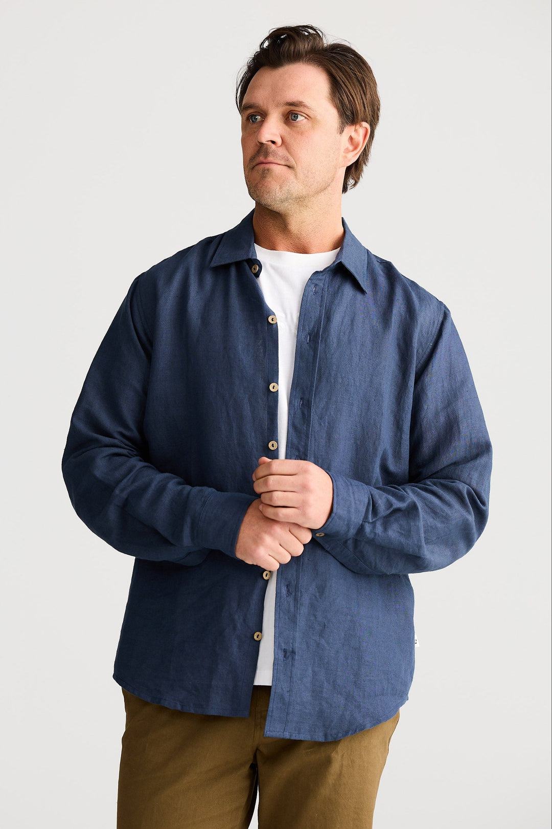 Man wearing a blue shirt over a white shirt with brown pants on a light gray background