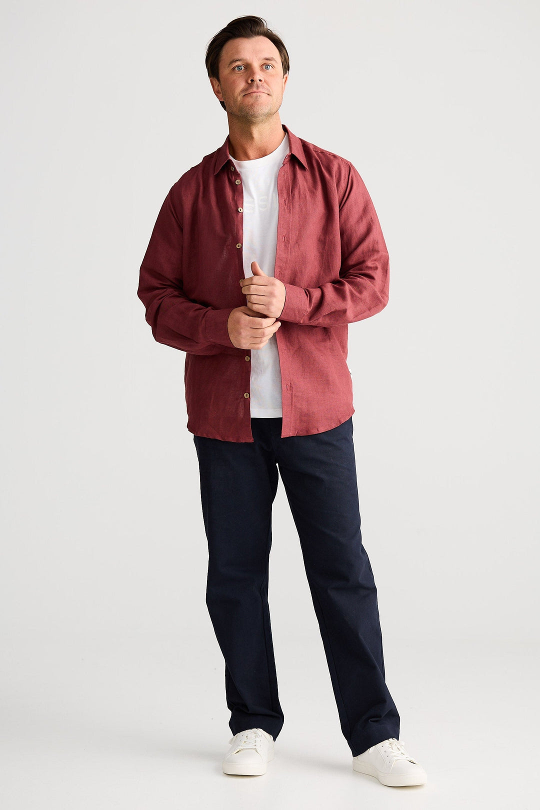 Man wearing a red shirt, white t-shirt, dark pants, and white shoes on a white background
