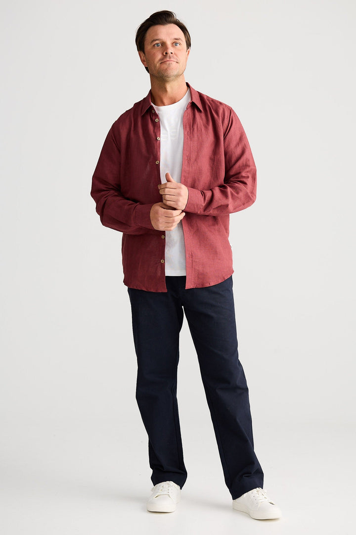 Man wearing a red shirt, white t-shirt, dark pants, and white shoes on a white background