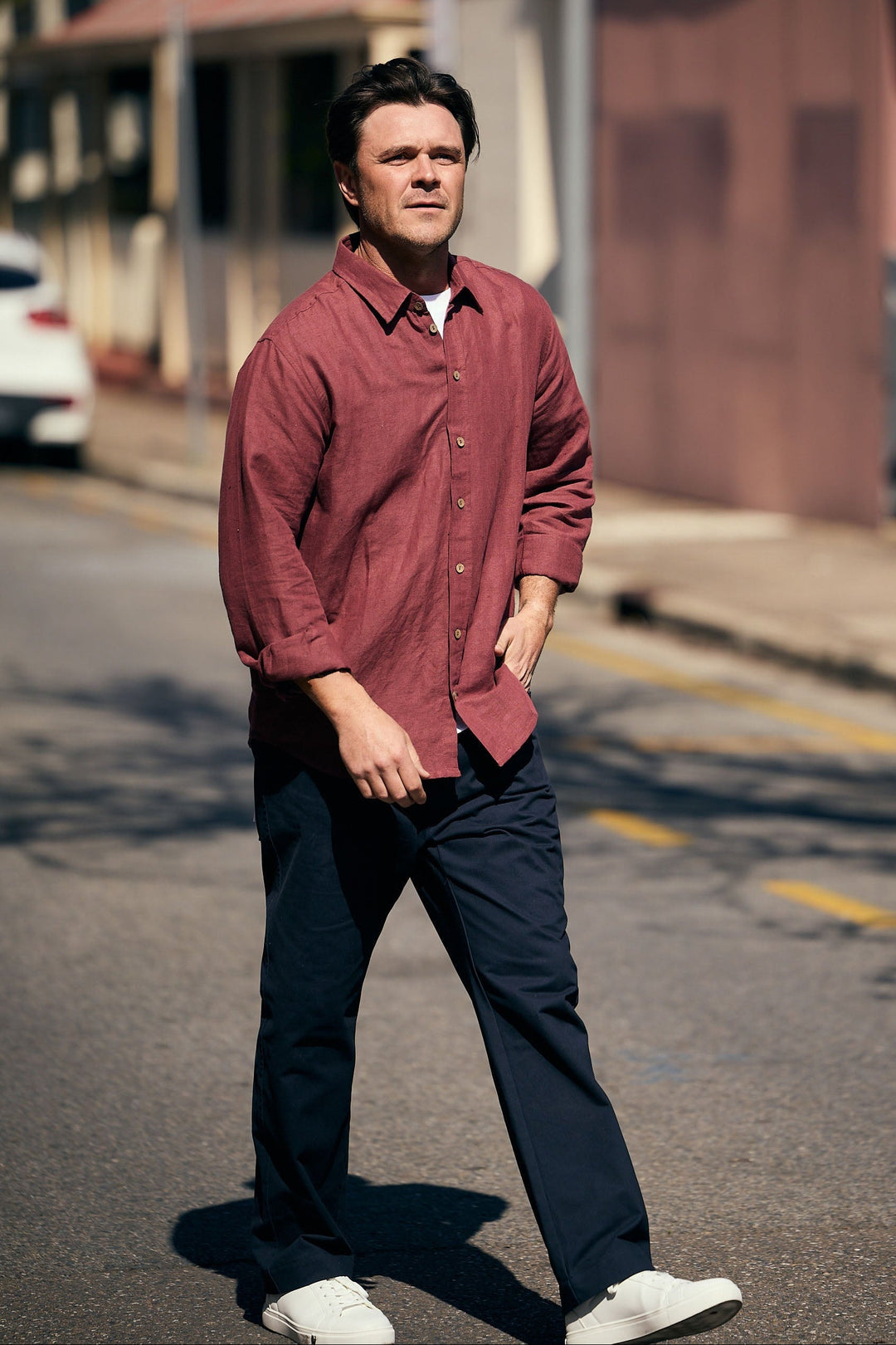 Man in a red shirt walking on a street with buildings in the background