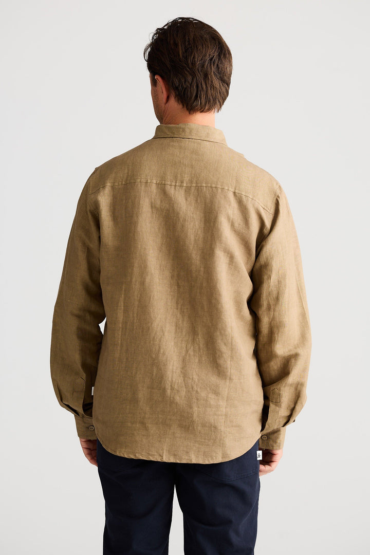 Man wearing a beige shirt and dark pants against a white background