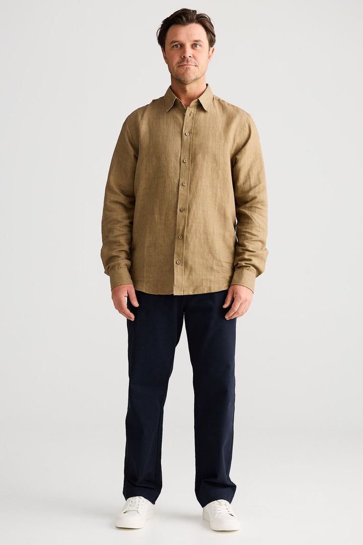 Man wearing a beige shirt and dark pants on a white background