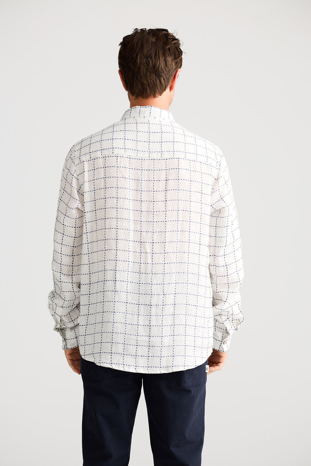 Man wearing a checkered shirt and dark pants on a white background