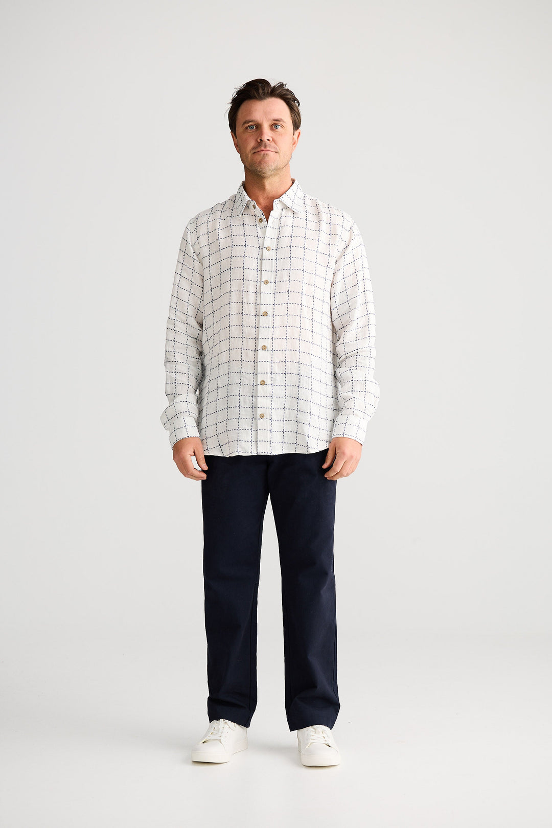 Man wearing a checkered shirt and dark pants on a white background