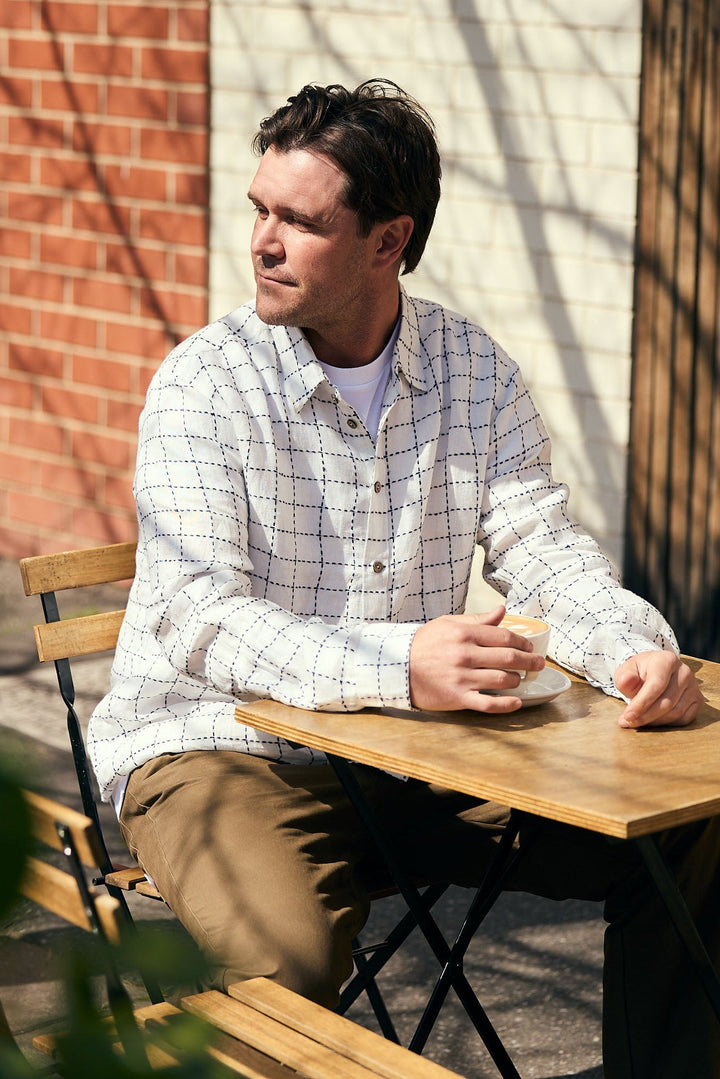 Man sitting at a wooden table outdoors with a brick wall and plants in the background