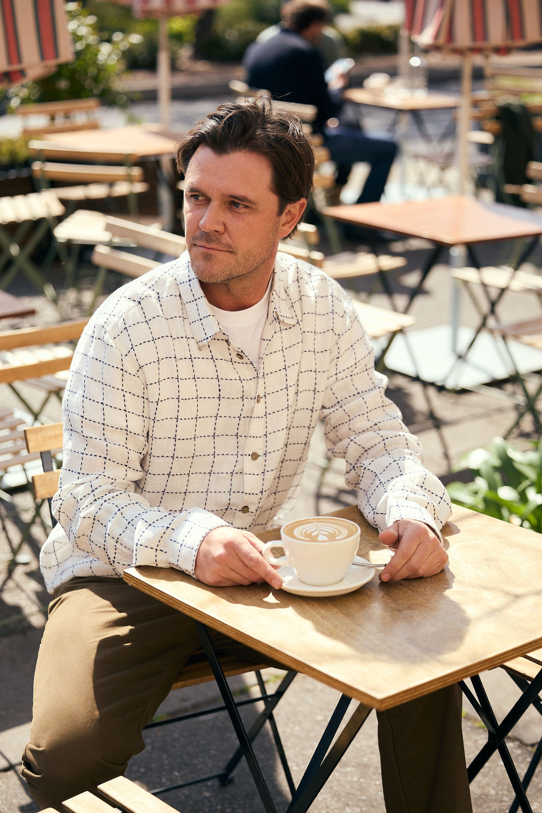 Man sitting at an outdoor cafe table with a cup of coffee