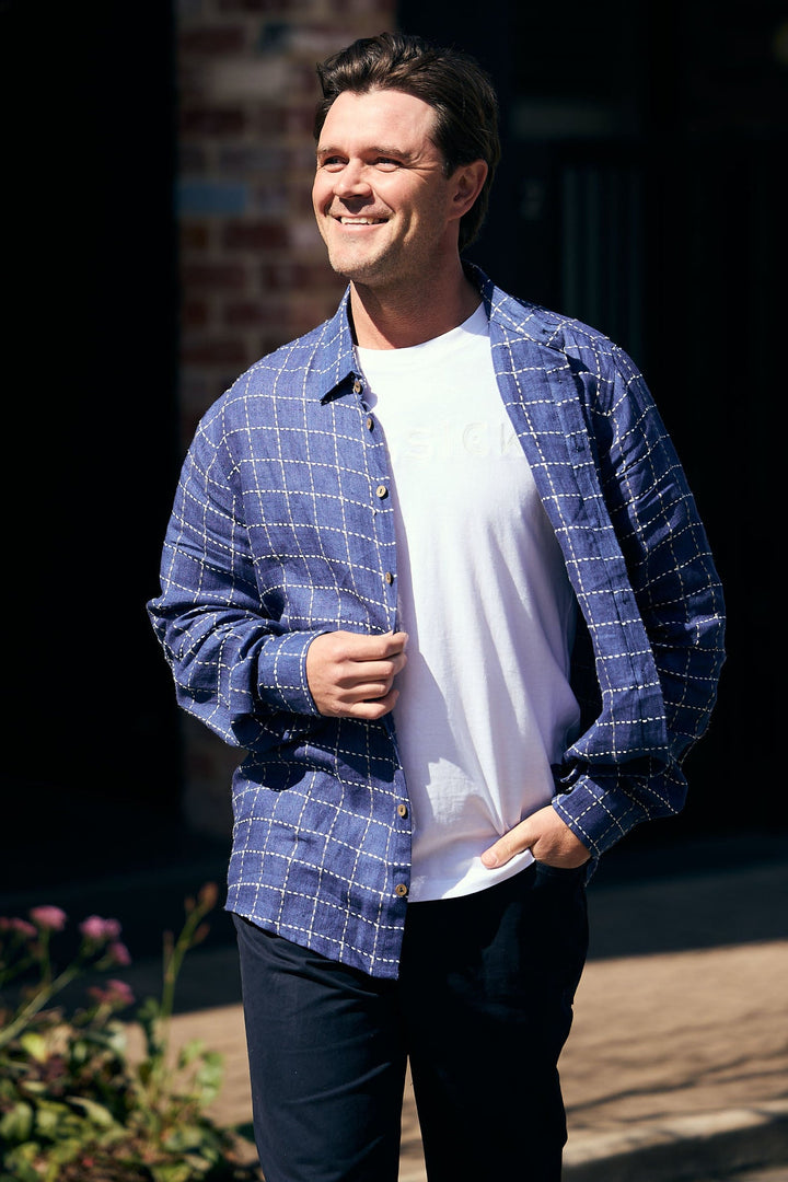 Man wearing a blue checkered shirt over a white t-shirt, standing outdoors.