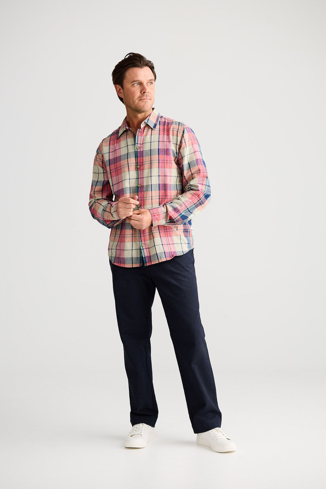 Man wearing a plaid shirt and dark pants on a white background
