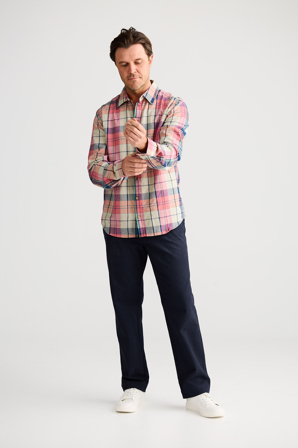 Man wearing a plaid shirt and dark pants on a white background
