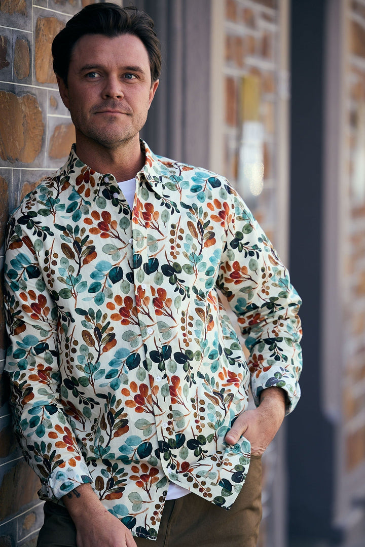 Man wearing a colorful floral shirt leaning against a brick wall.