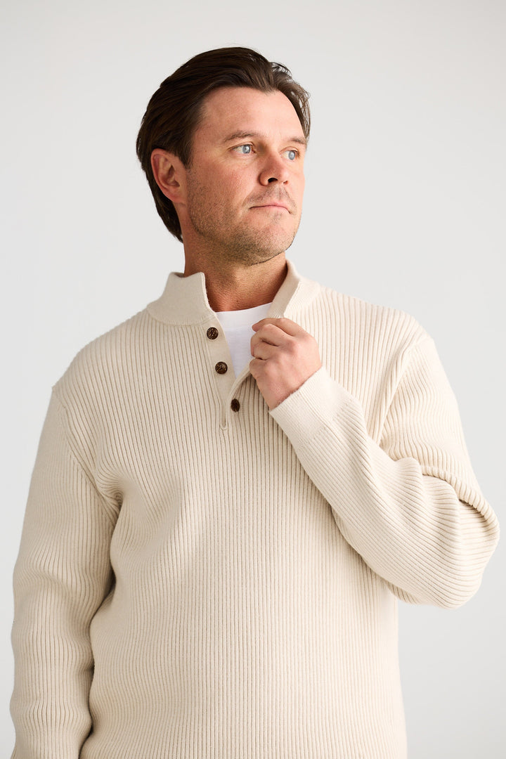 Man wearing a beige ribbed sweater against a plain background