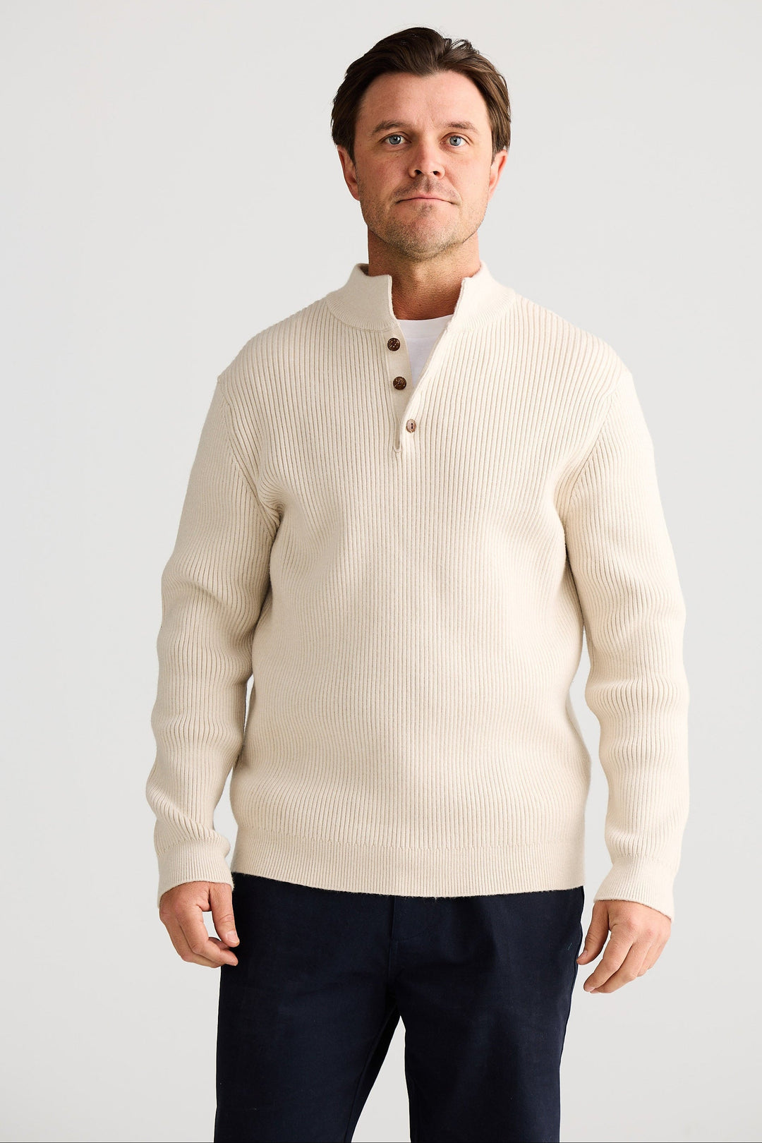 Man wearing a cream cardigan over a white shirt with navy pants on a light gray background