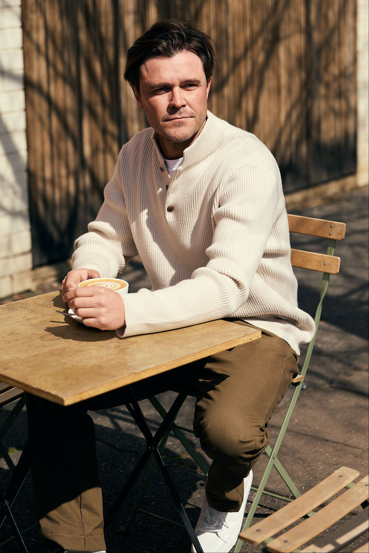 Man sitting at a wooden table outdoors holding a cup.