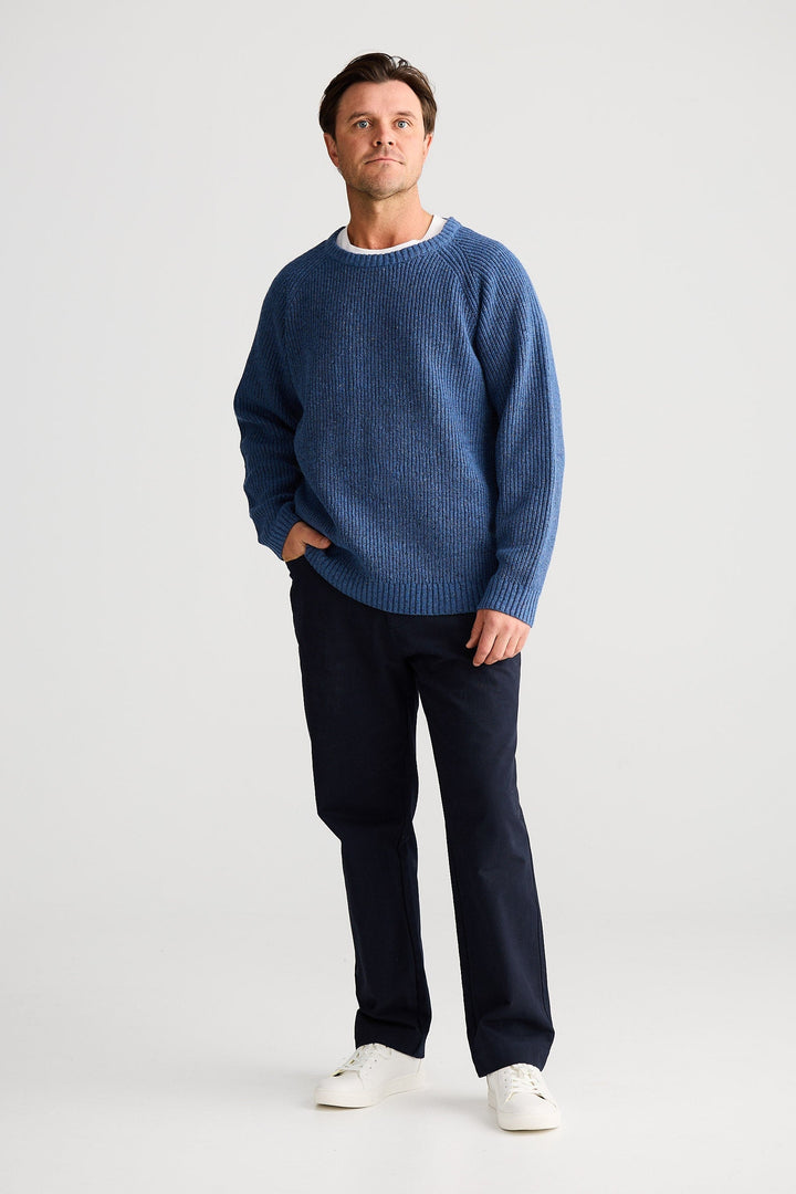 Man wearing a blue sweater and dark pants on a white background