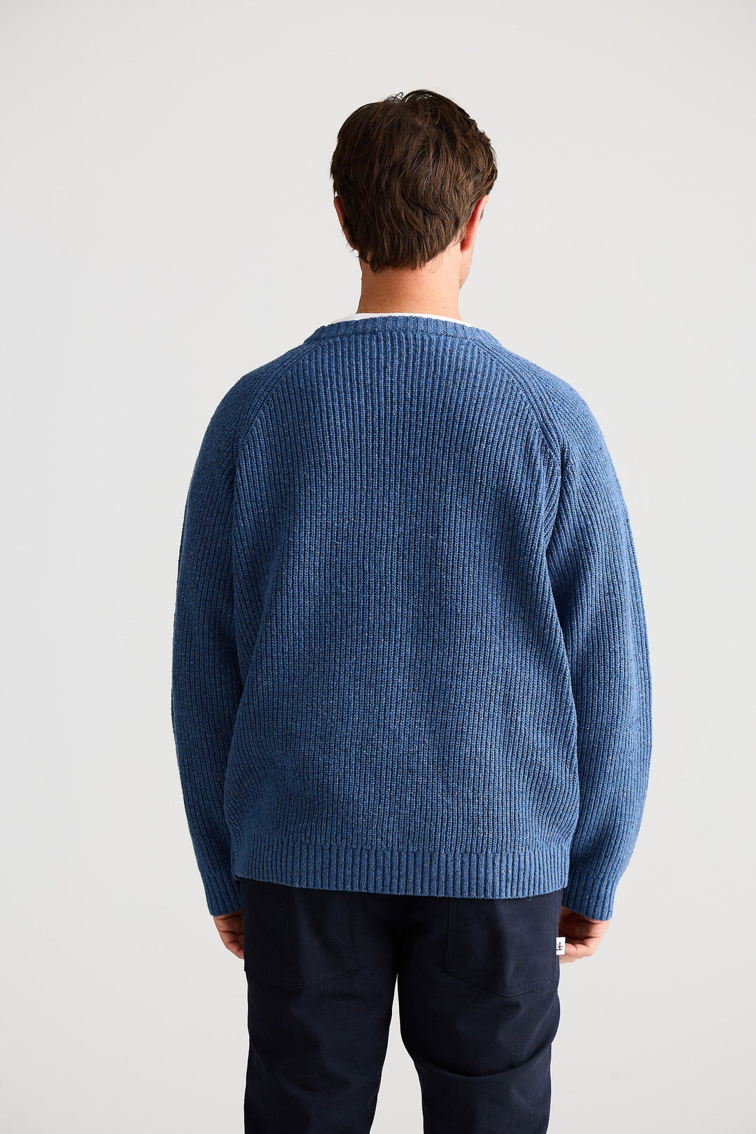 Person wearing a blue sweater from behind on a light gray background