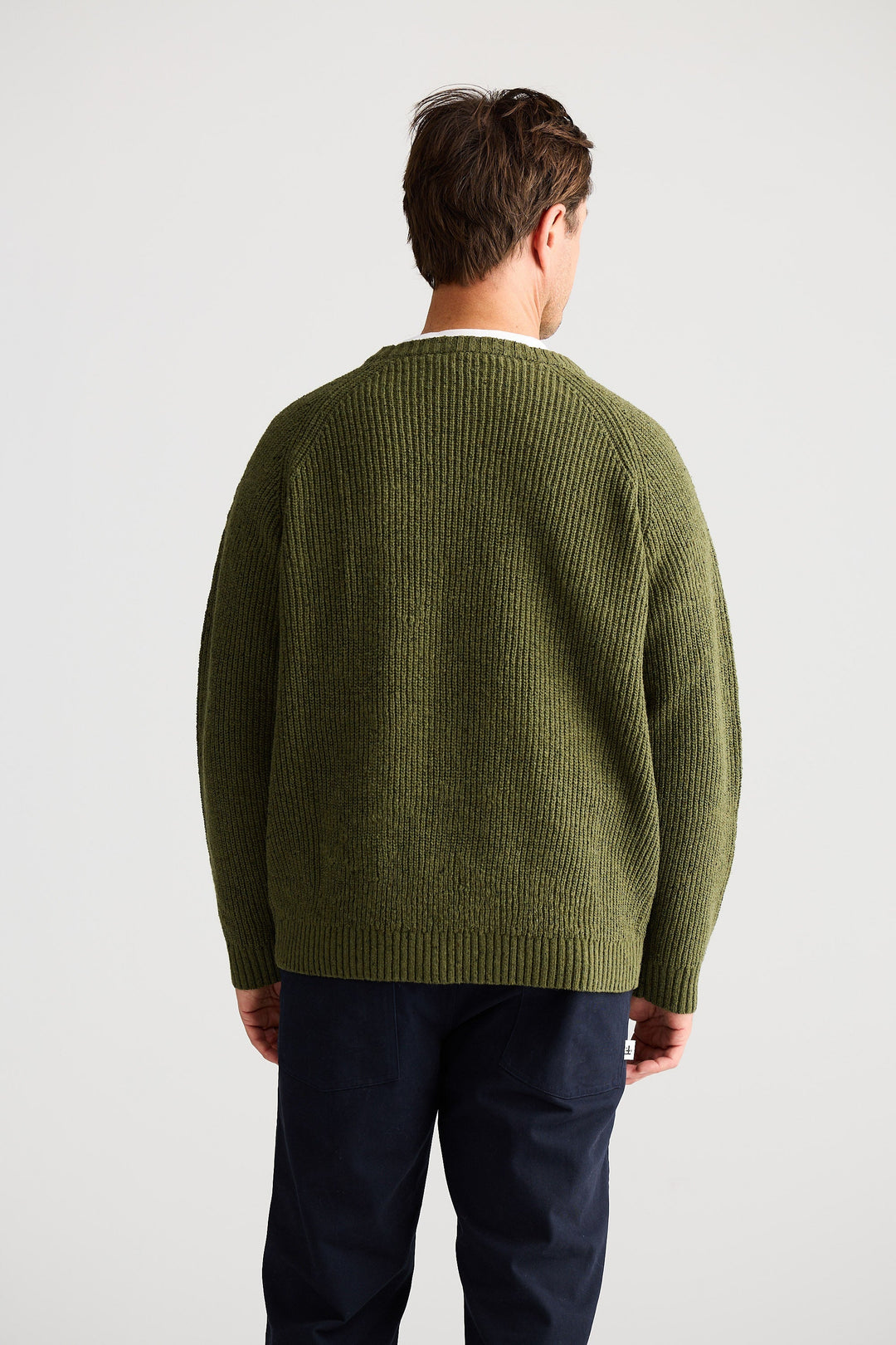 Man wearing a green sweater and dark pants on a light gray background