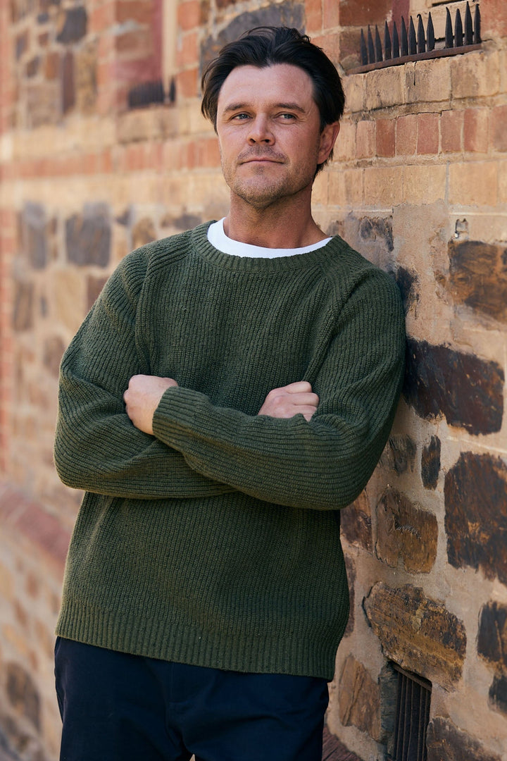 Man standing against a brick wall wearing a green sweater