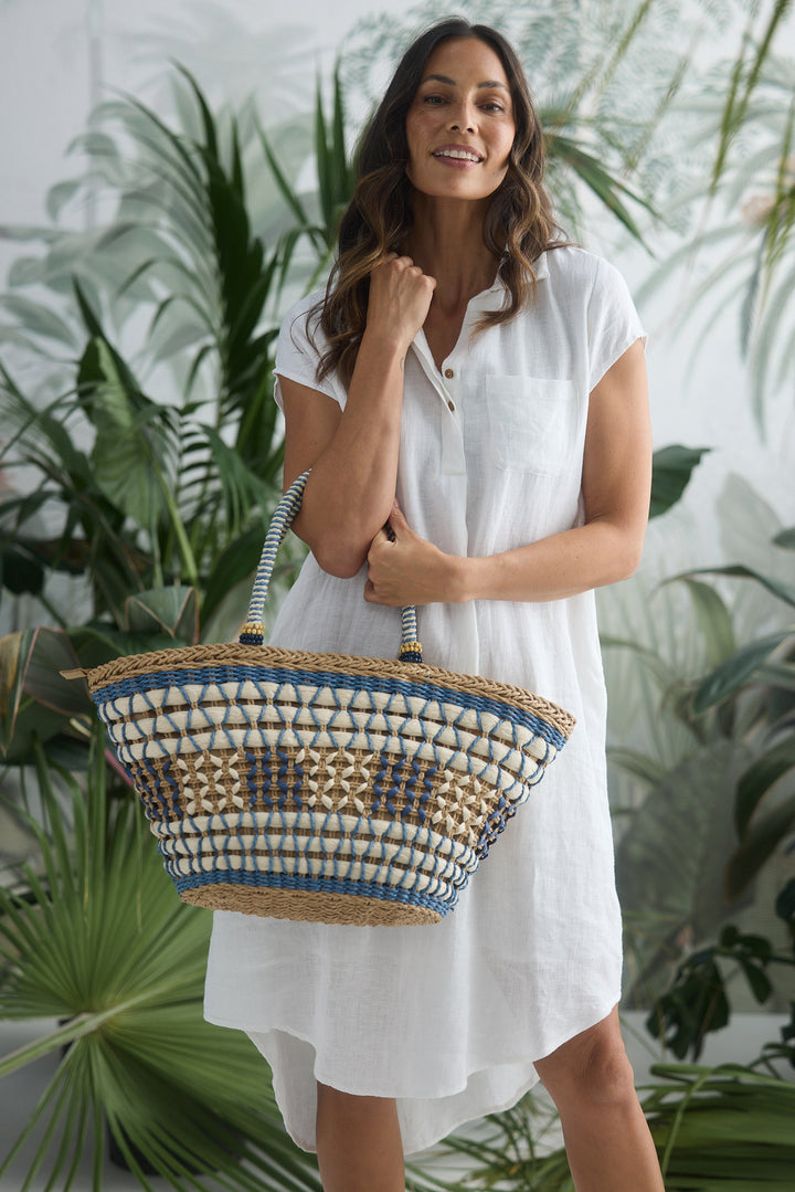 Woman in a white dress holding a woven bag with plants in the background