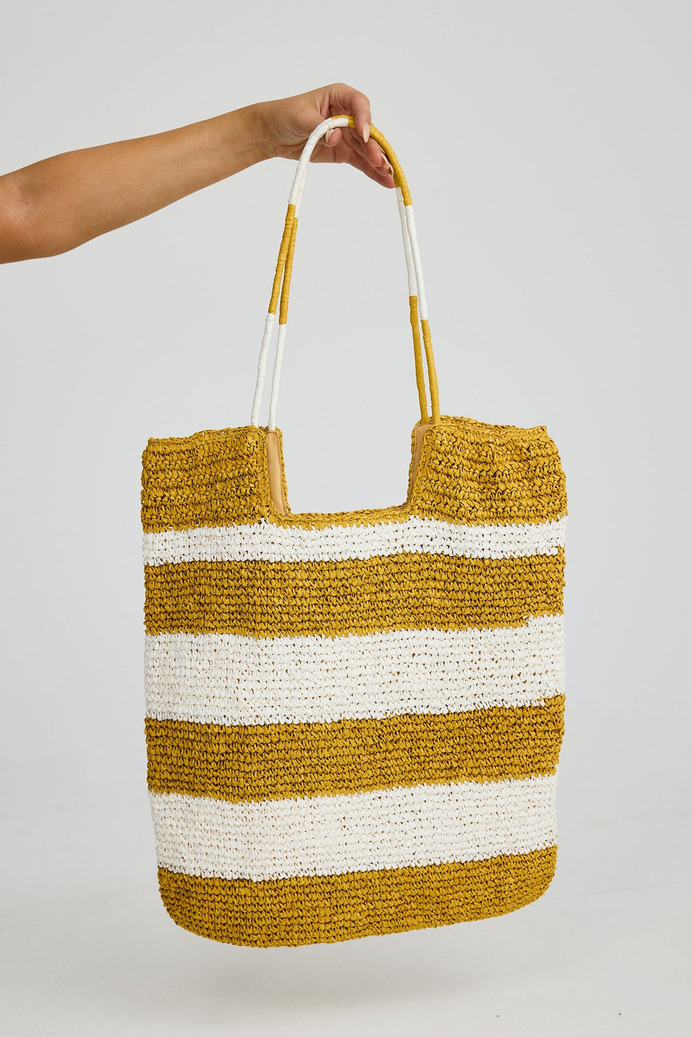 Hand holding a striped yellow and white woven bag against a plain background