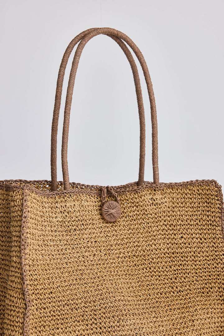 Brown woven tote bag with a button on a light gray background