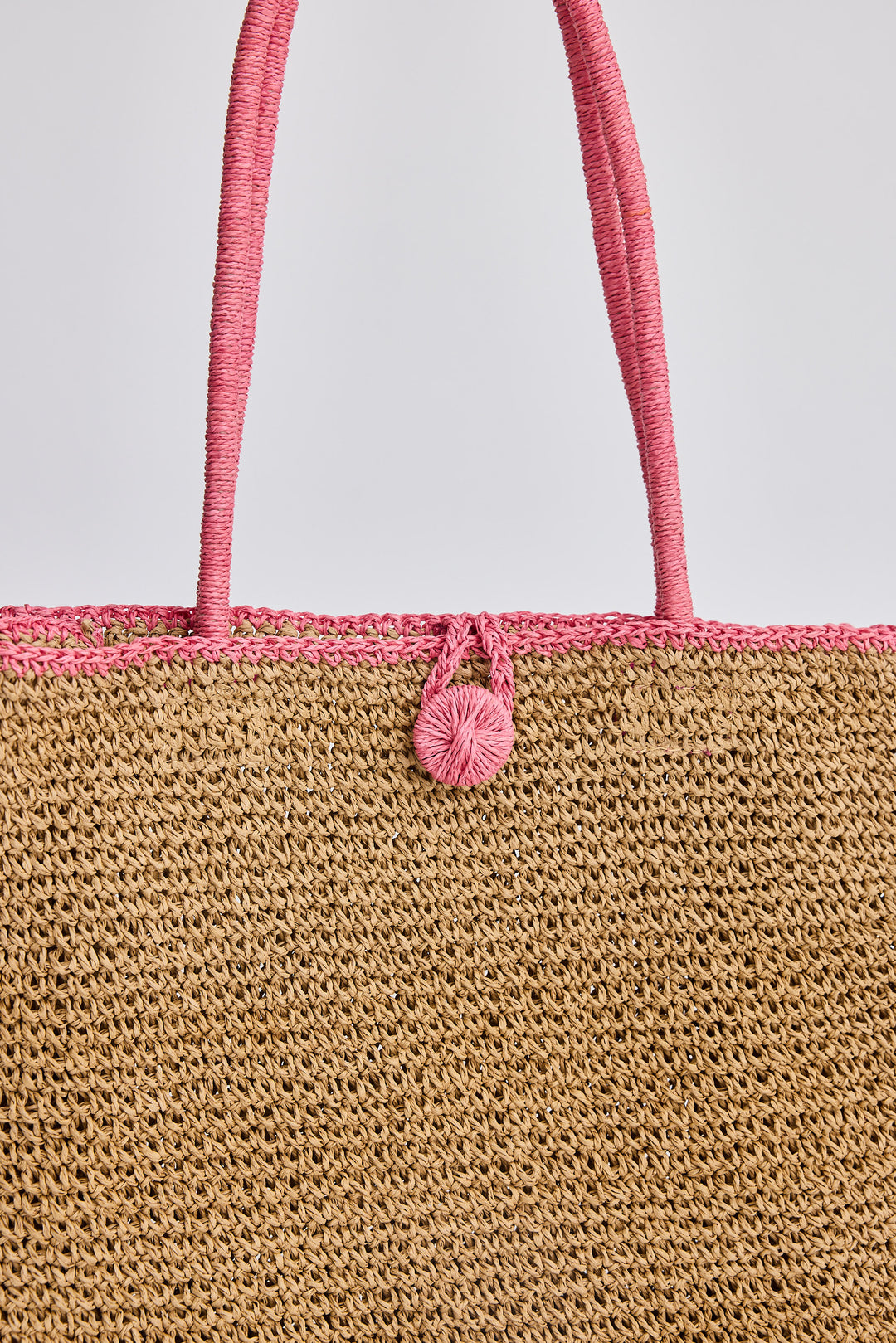 Close-up of a woven bag with pink handle and decorative element on a light gray background
