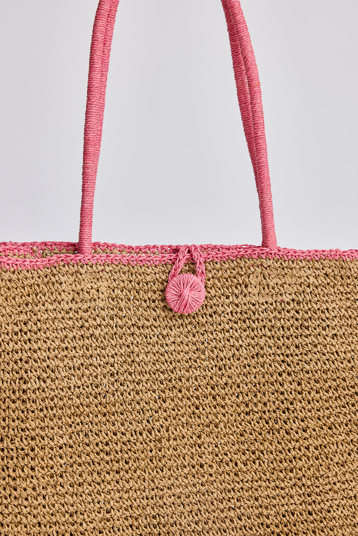 Close-up of a woven bag with pink handle and decorative element on a light gray background