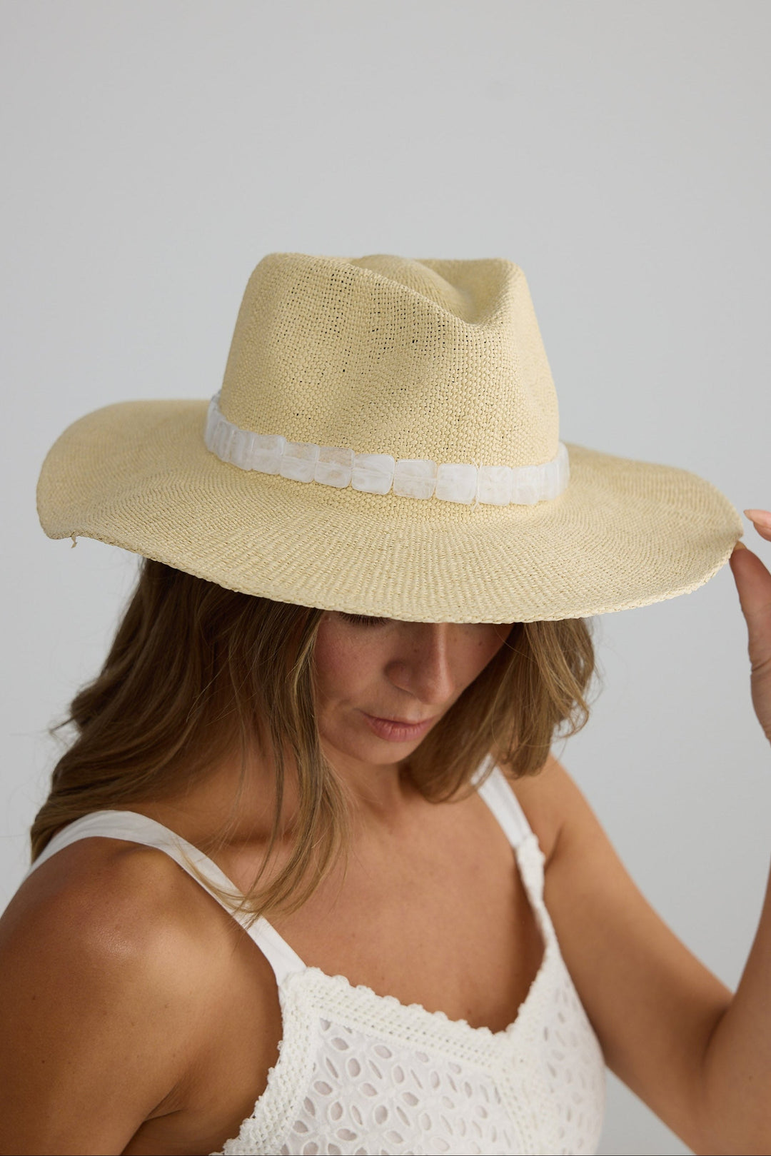 Woman wearing a beige straw hat with a white band on a plain background