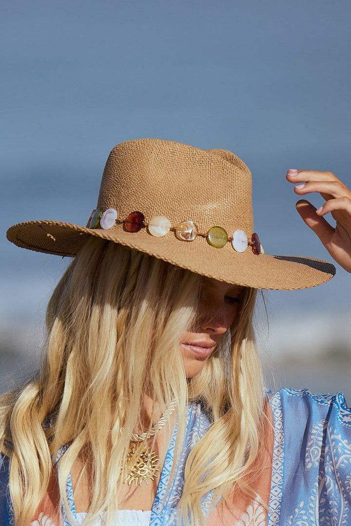 Woman on a beach wearing a wide-brimmed hat and a patterned scarf.