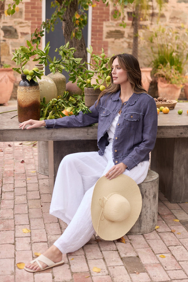 Woman sitting outdoors with a hat, surrounded by plants and fruit