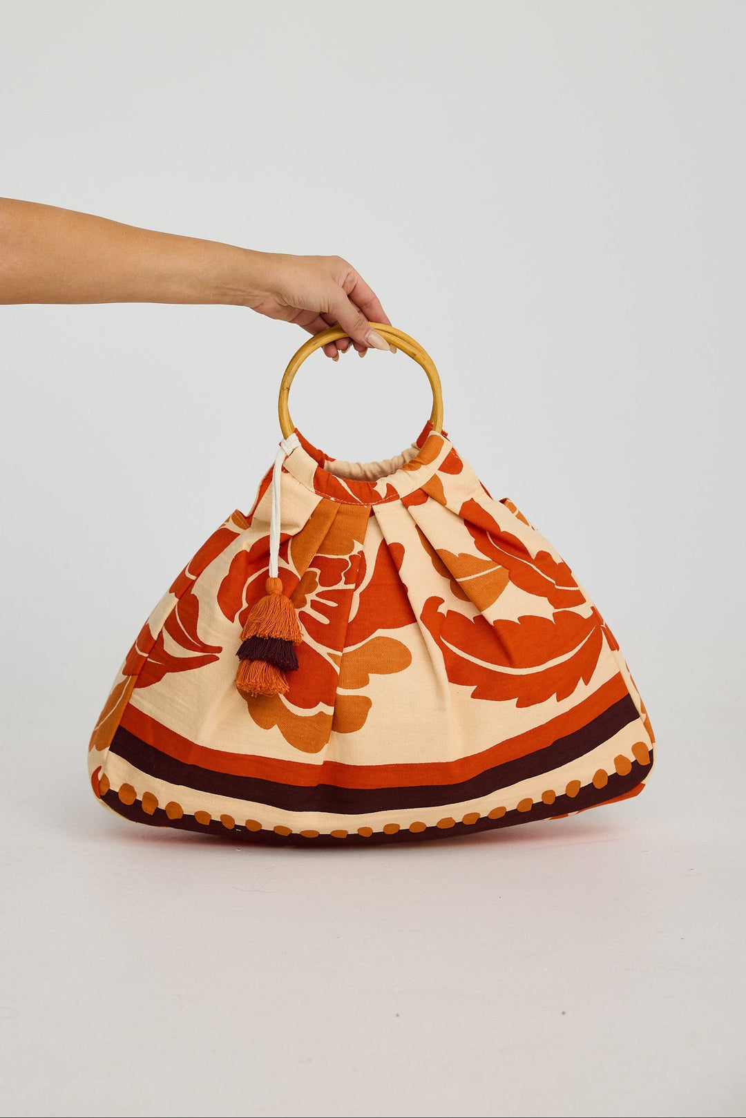 Bag with floral pattern and circular cane handle held by a hand on a white background