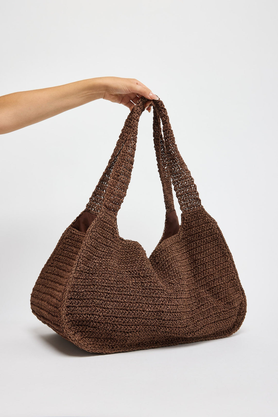 Large slouchy hobo bag in chunky chocolate brown woven raffia with braided rope handles, held by hand against a white background