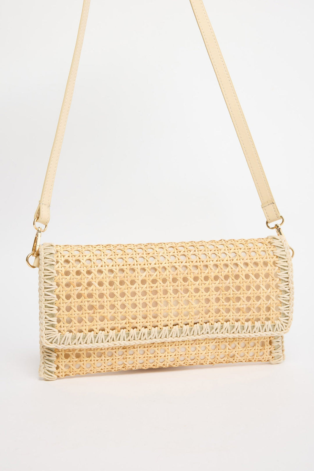 Rectangular fold-over crossbody bag in natural rattan cane weave with cream whipstitched trim along all edges and a cream leather adjustable strap with gold-tone hardware, shown against a white background