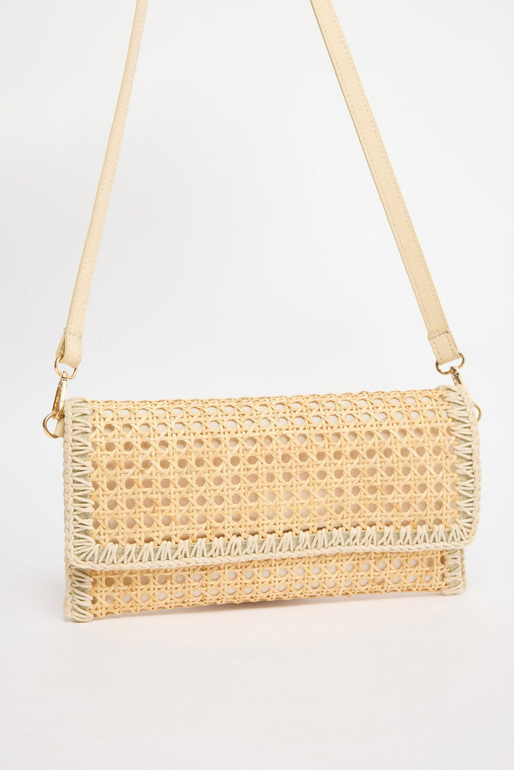 Rectangular fold-over crossbody bag in natural rattan cane weave with cream whipstitched trim along all edges and a cream leather adjustable strap with gold-tone hardware, shown against a white background