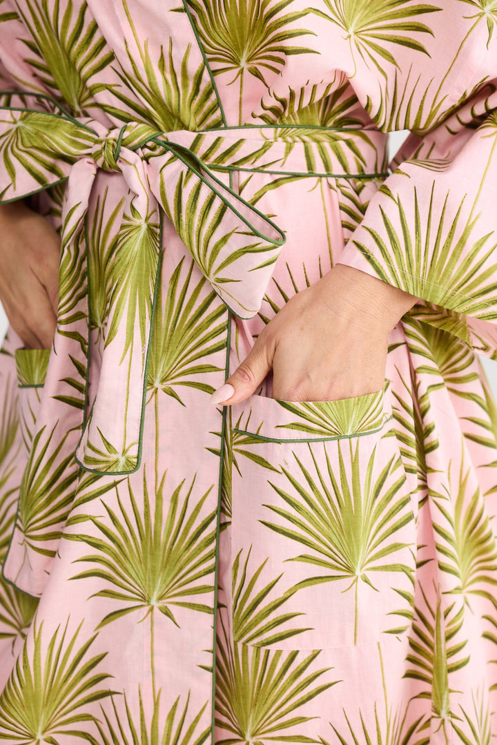 Pink robe with green palm leaf pattern worn by a person.