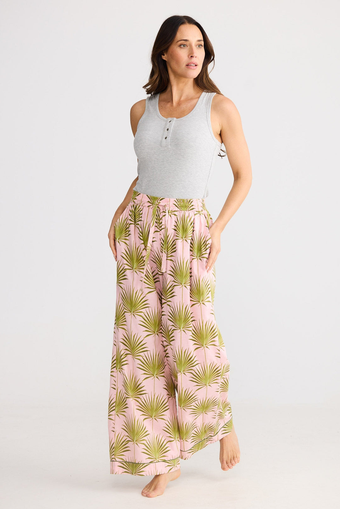 Woman wearing a light gray sleeveless top and pink palm leaf patterned pants on a white background