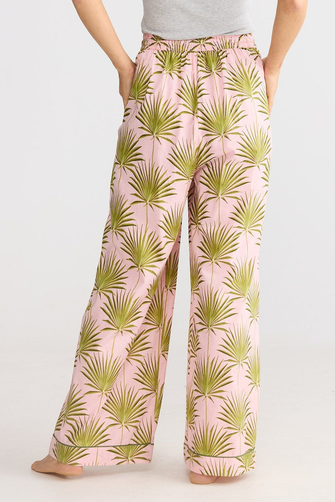 Woman wearing pink palm leaf patterned pants on a white background