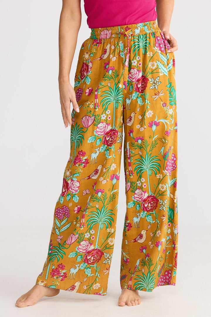 Person wearing a pink top and floral-patterned mustard yellow pants on a white background