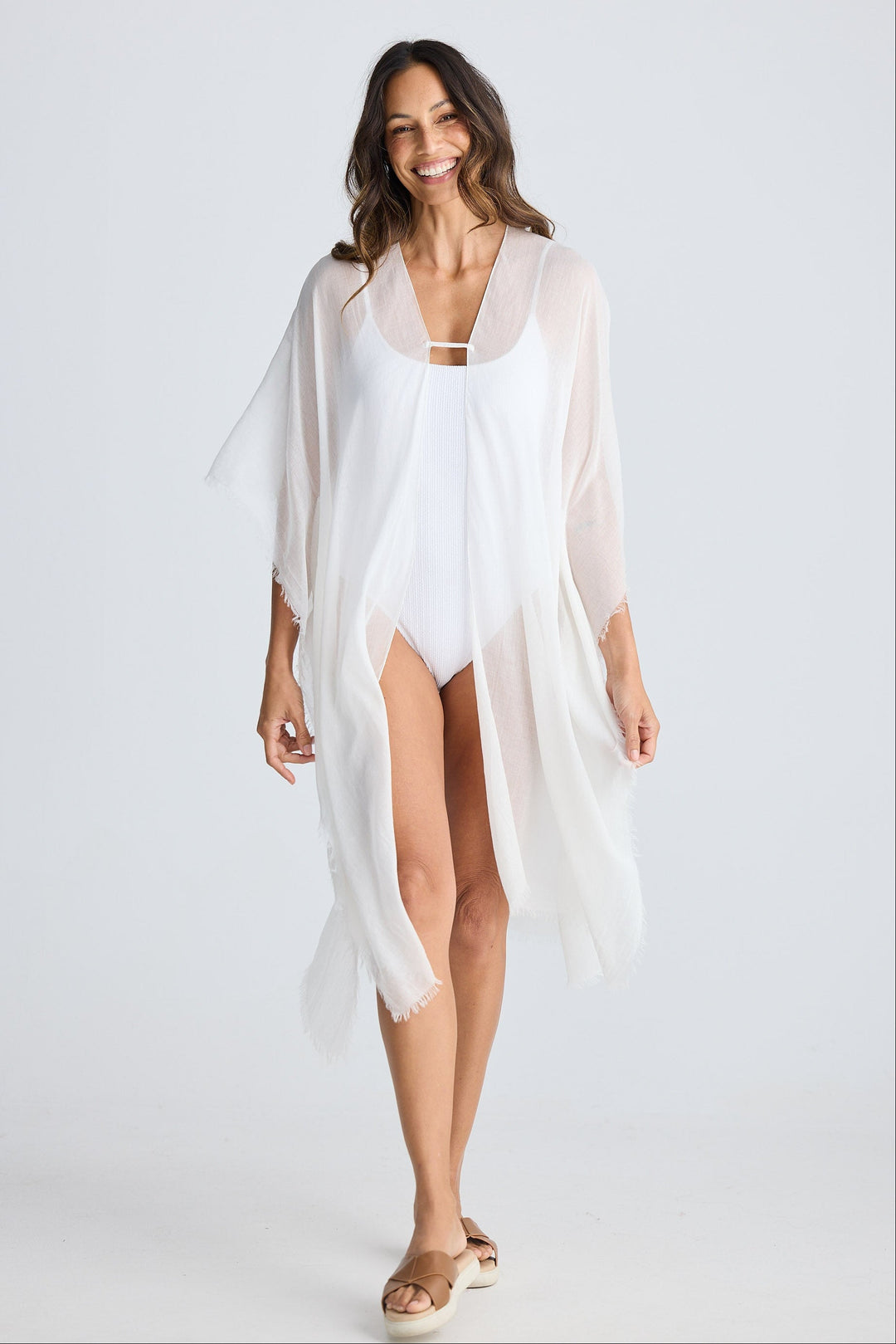 Woman wearing a white cover-up over a swimsuit on a plain background