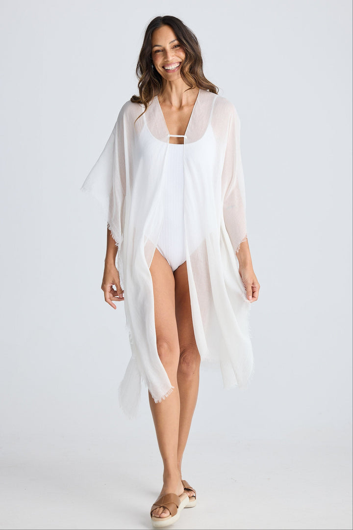 Woman wearing a white cover-up over a swimsuit on a plain background