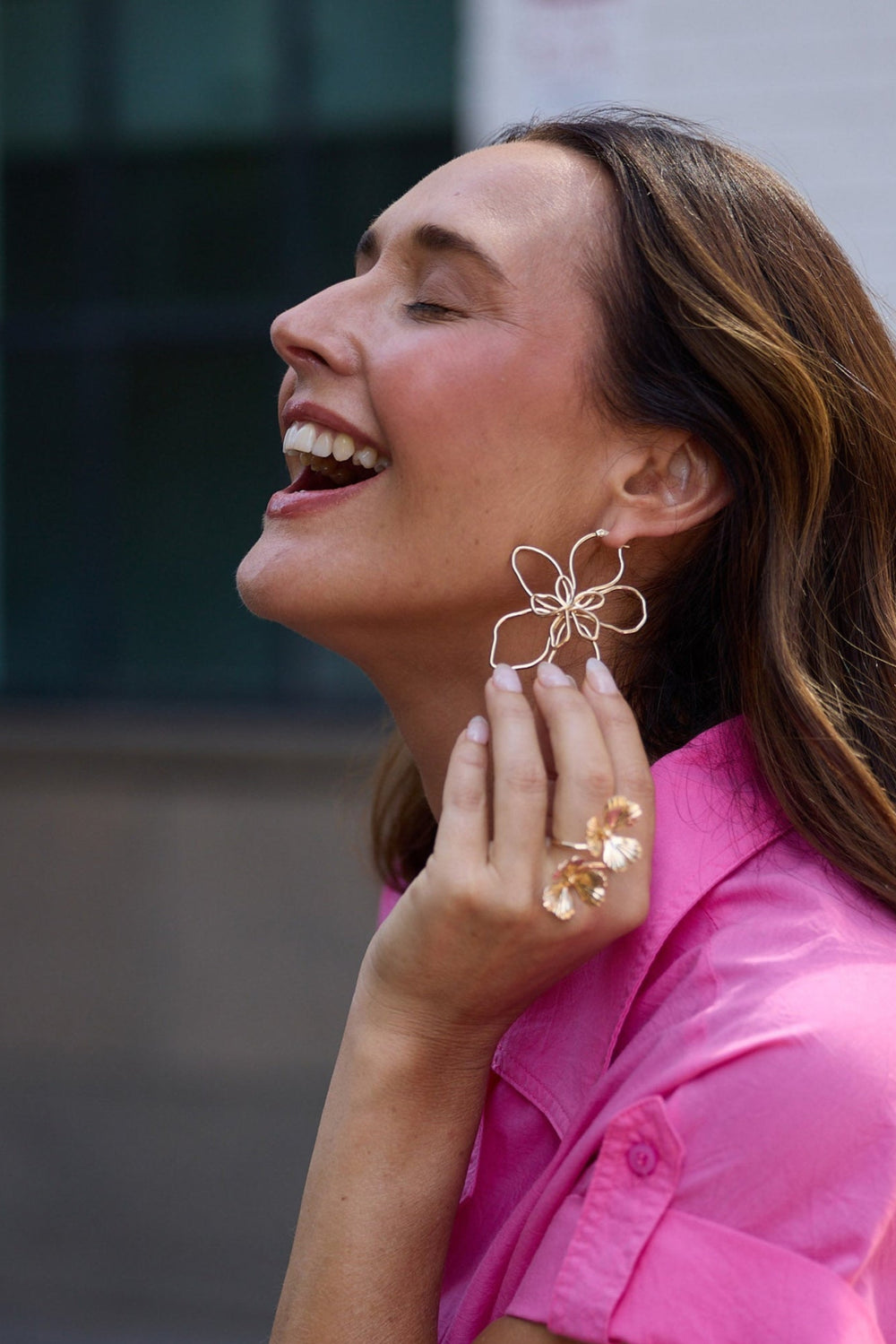 Woman in a pink dress wearing gold earrings and rings outdoors.